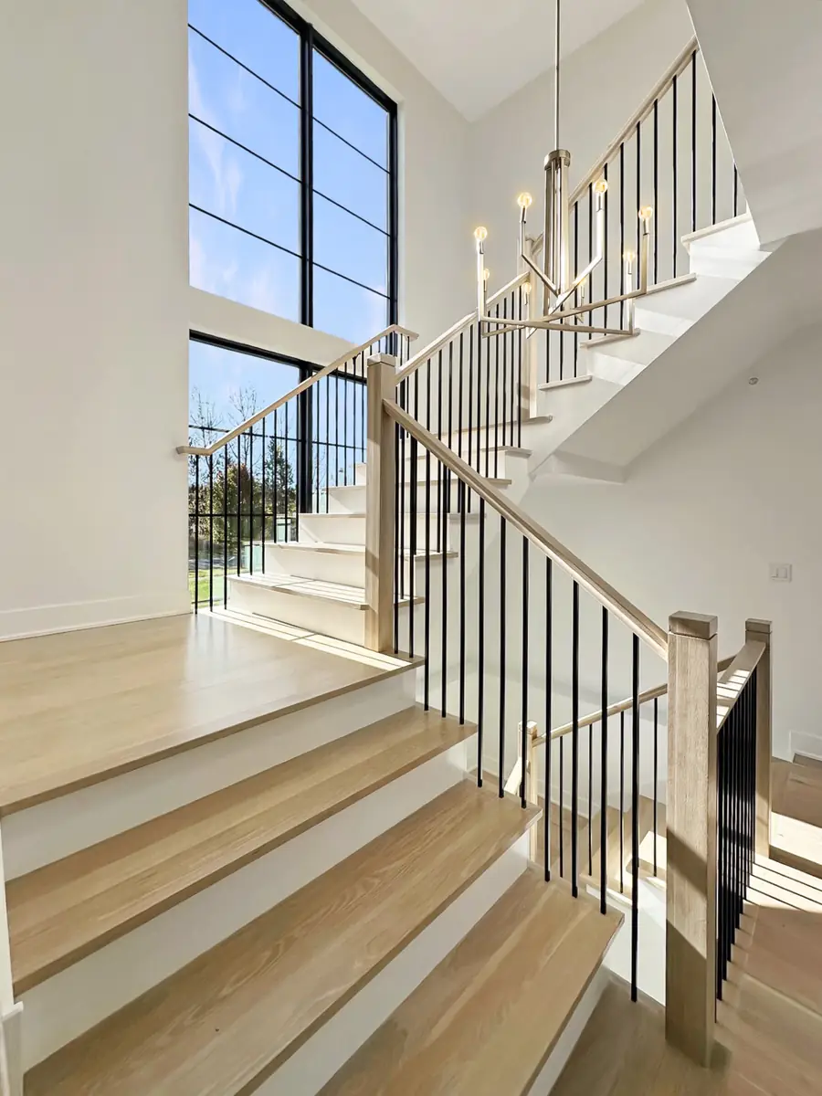 White oak staircase with black metal balusters and tall windows in a Skycrest custom home