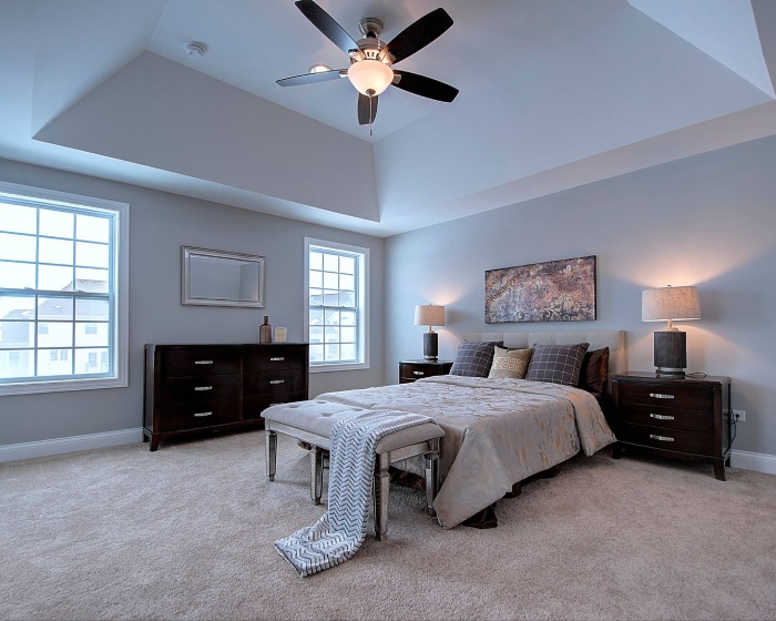 A well-decorated bedroom with a ceiling fan above a neatly made bed, illustrating a potential home addition design.