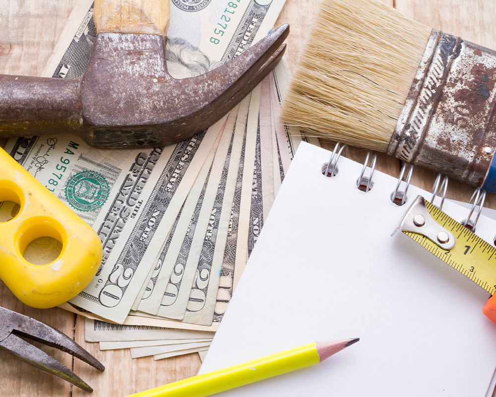 A wooden table displays a pile of tools alongside cash, symbolizing budget-friendly bathroom remodeling planning.
