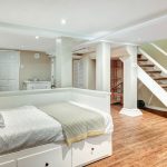 A stylish basement bedroom with a white bed and stairs, illustrating remodeling concepts for homes in Naperville.