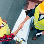 Two construction workers engage in a handshake on a construction site, highlighting teamwork in custom home building projects.